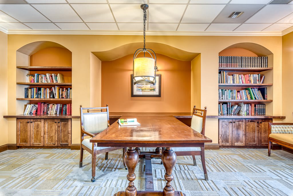 A cozy library reading room with a wooden table and chairs, surrounded by bookshelves filled with books.