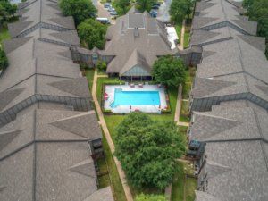 Aerial view of an apartment complex featuring a central swimming pool surrounded by buildings and trees.