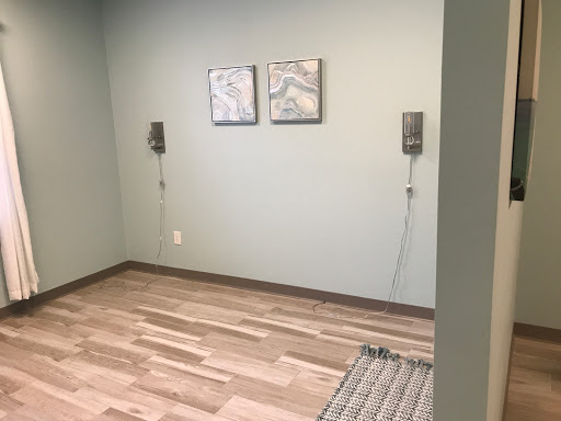 A minimalist interior room featuring light green walls, wooden flooring, and two wall-mounted speakers.