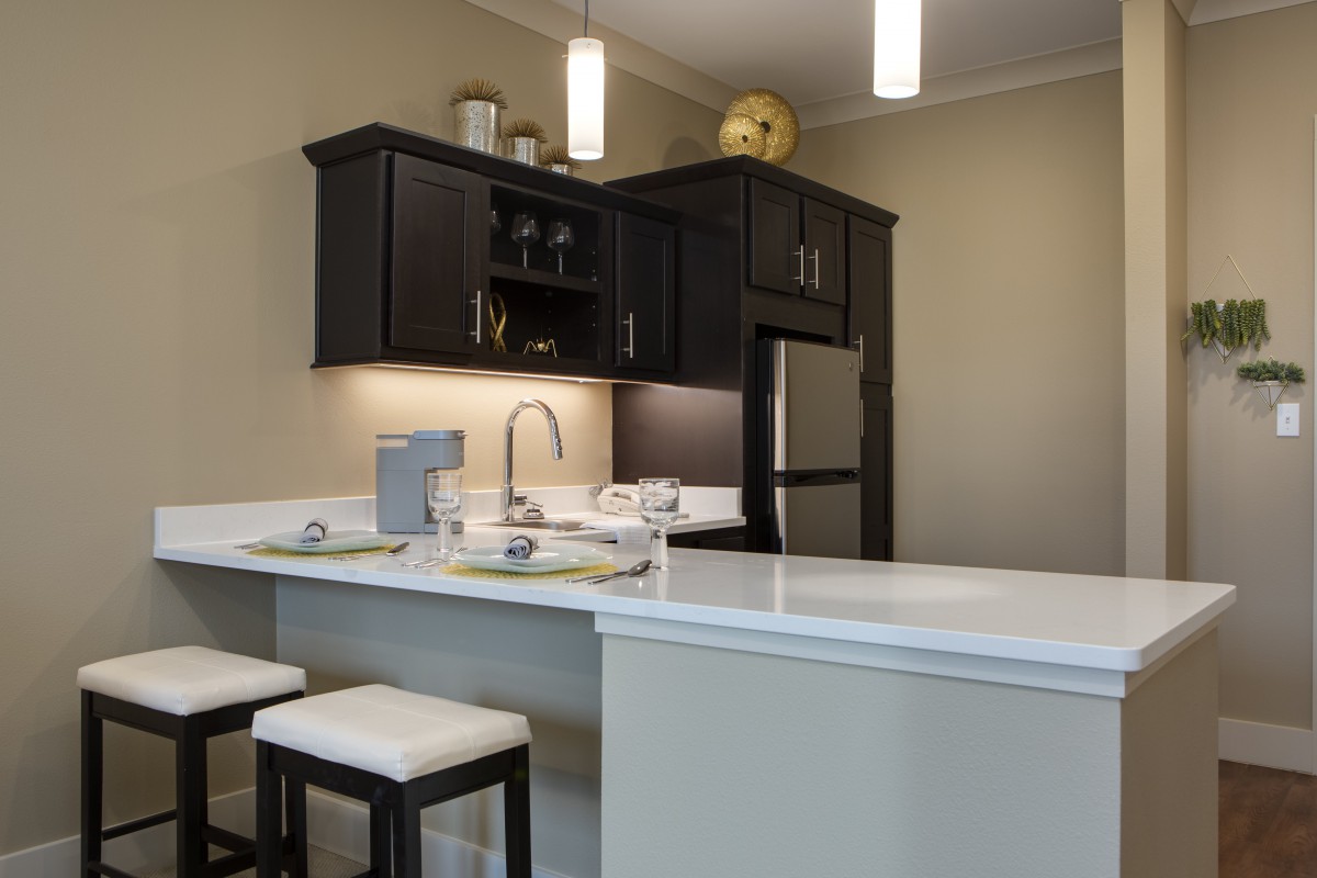 A modern kitchen with dark cabinetry and a sleek white countertop featuring bar stools.