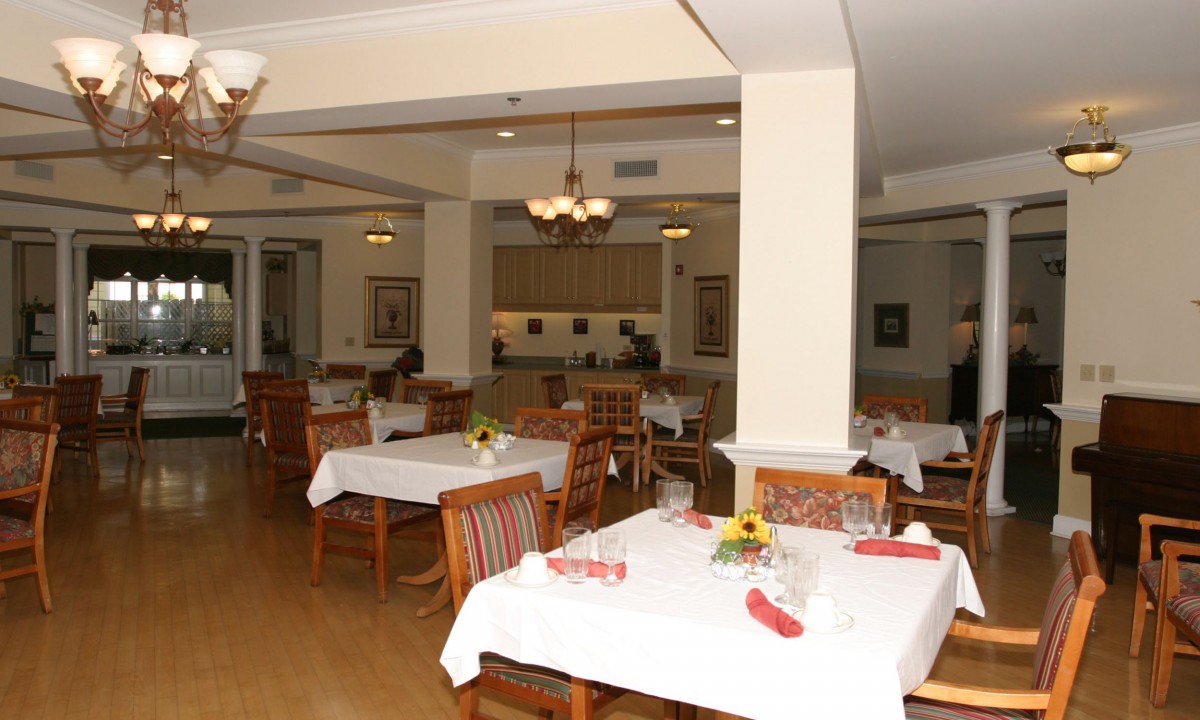 An empty dining room with neatly set tables and chairs, illuminated by warm indoor lighting.