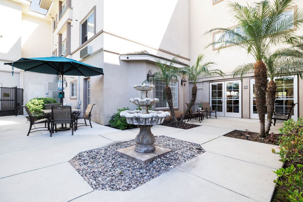 A serene courtyard with a central fountain, surrounded by outdoor seating and palm trees.