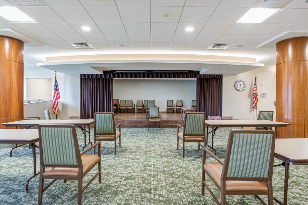 A small conference room with a stage, chairs arranged in rows, and flags on either side.