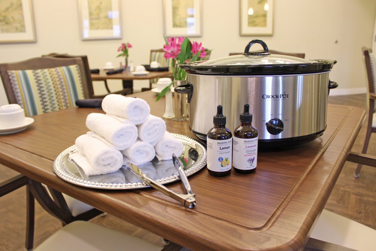 A cozy spa setup with rolled towels, essential oils, and a slow cooker on the table.