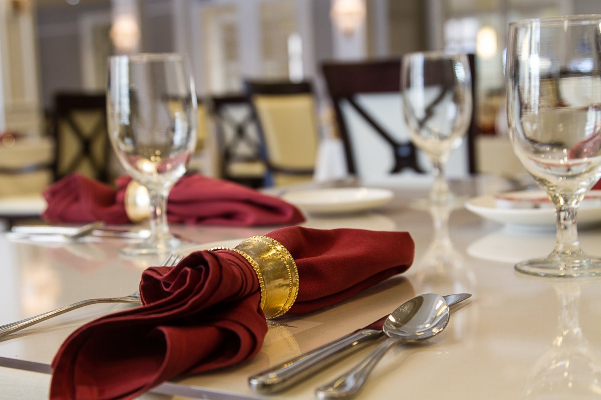 A beautifully set dining table in a restaurant with red napkins and crystal glasses.