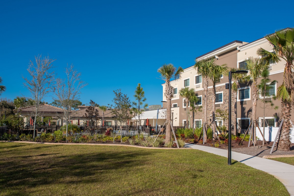 A modern apartment complex surrounded by palm trees and a well-maintained grass lawn on a sunny day.