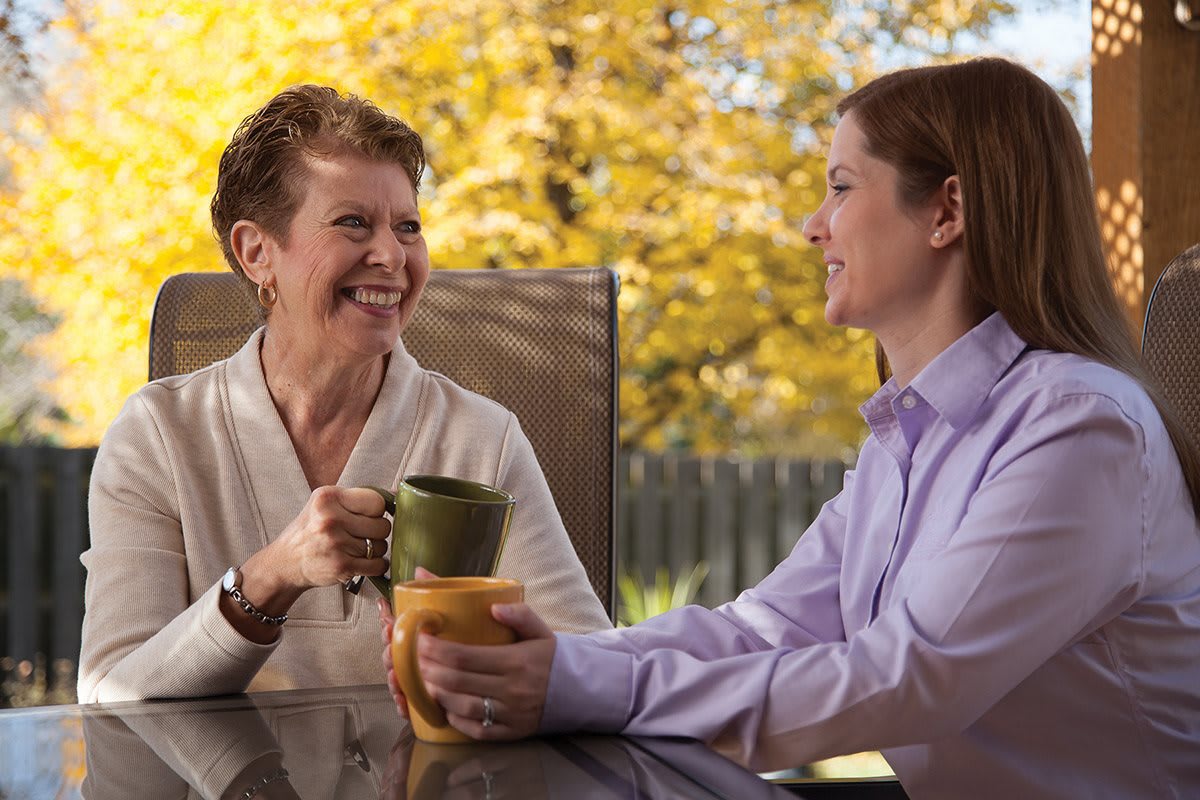Two people enjoying a conversation over coffee in a sunny autumn setting.