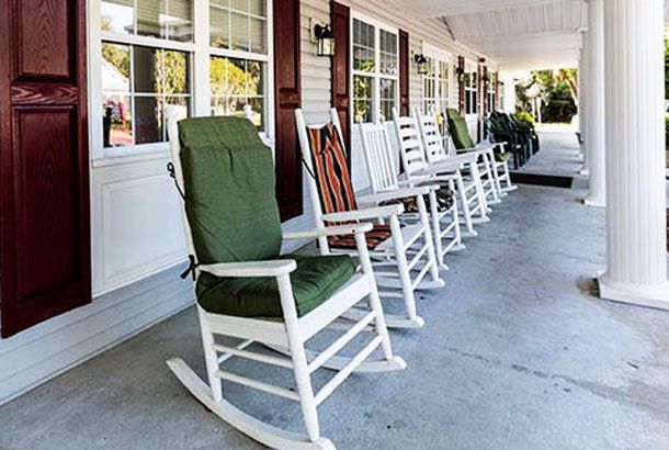 A row of rocking chairs with cushions lined up on a porch, offering a cozy outdoor seating area.