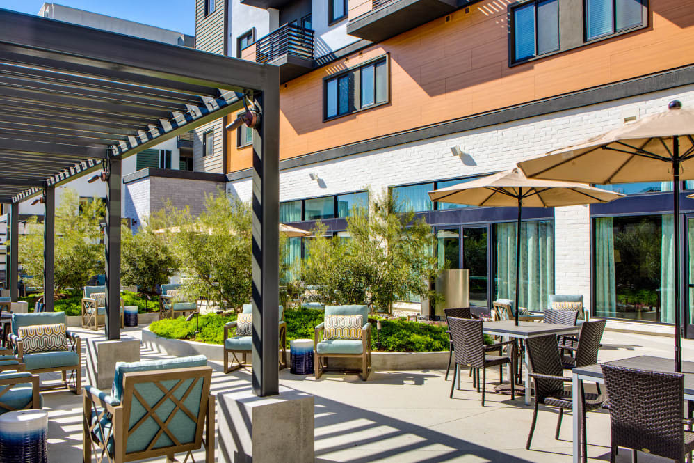 A modern apartment courtyard with outdoor seating and a pergola under sunny skies.