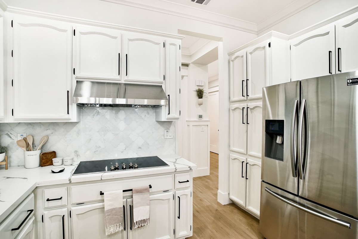A modern kitchen featuring white cabinets, a sleek cooktop, and stainless steel appliances.