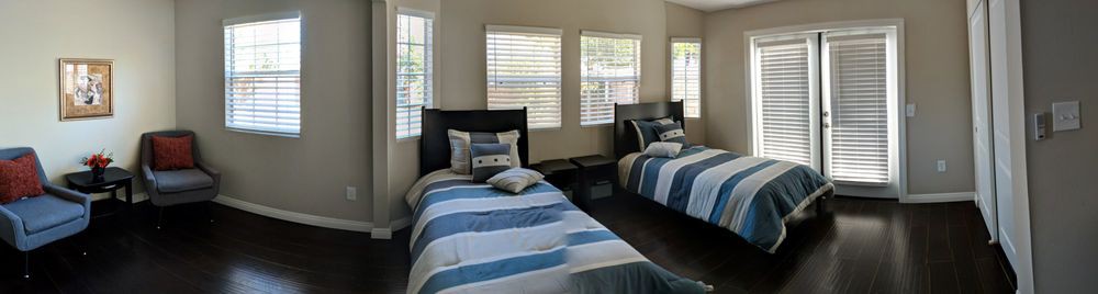 A cozy bedroom featuring two twin beds with striped bedding and ample natural light from the windows.