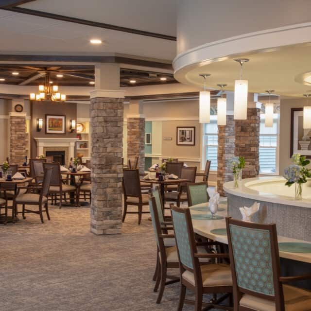 A spacious and elegantly designed dining area with multiple tables and chairs, featuring modern lighting and stone columns.