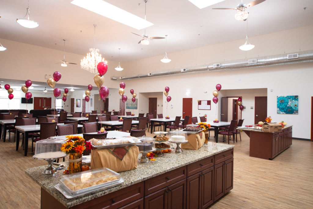 A spacious dining hall decorated with balloons and set up for an event, featuring neatly arranged tables and a central counter.