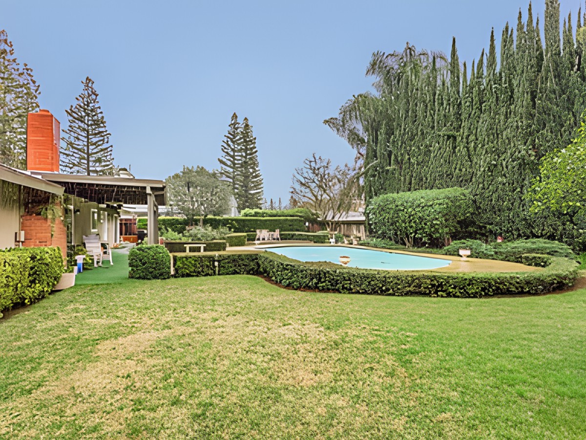 A spacious backyard featuring a swimming pool surrounded by lush greenery and well-maintained hedges.
