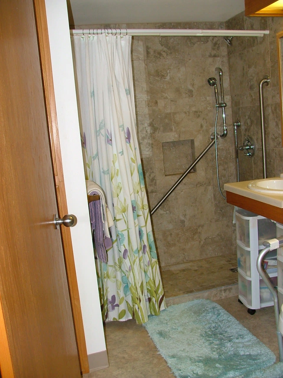 A bathroom with a shower area, floral curtain, and sink.