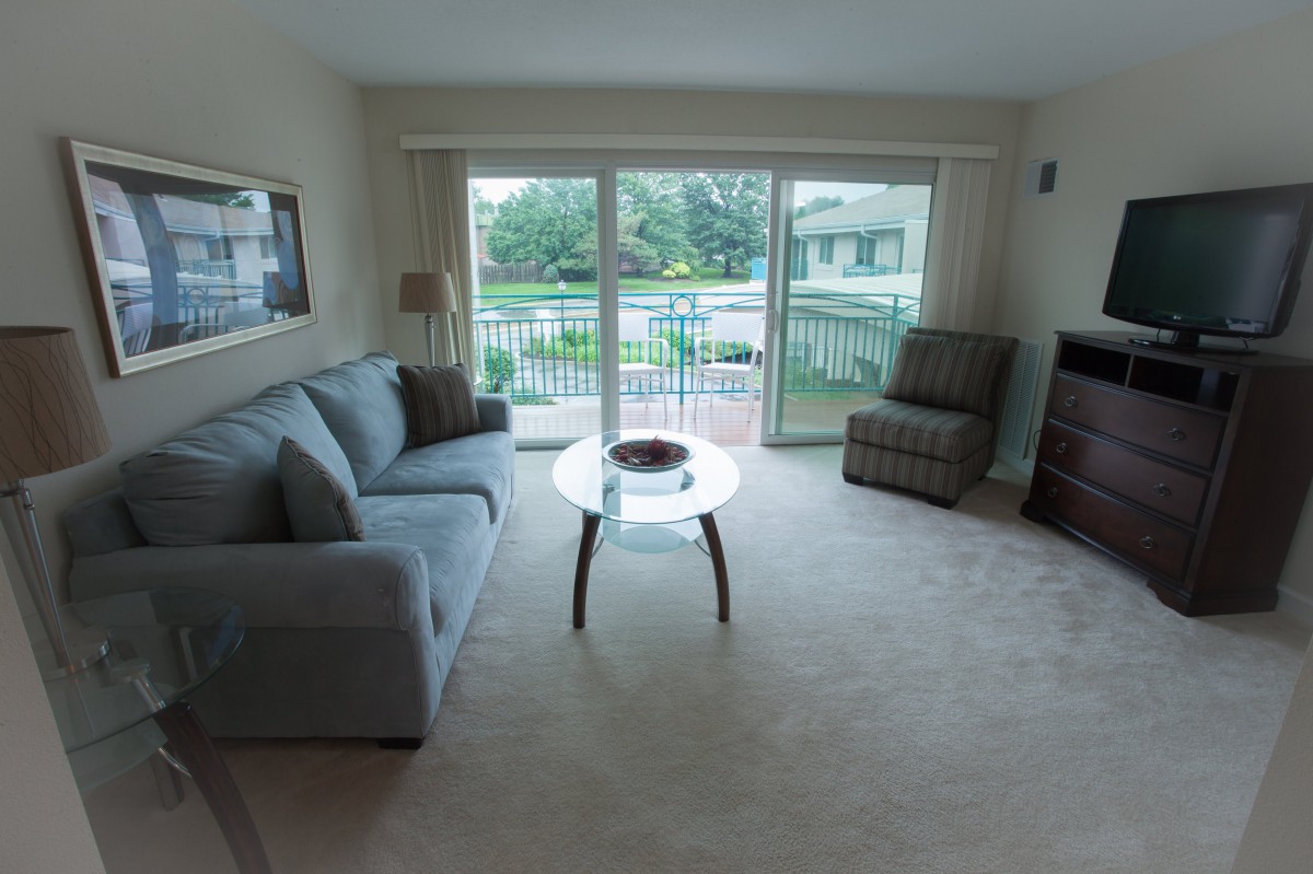A cozy living room with a sofa, coffee table, and a chair facing a sliding glass door with an outdoor view.