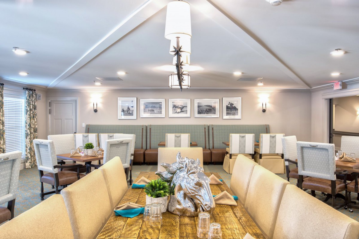 A modern dining room with a long table, upholstered chairs, and elegant lighting, showcasing framed art on the walls.