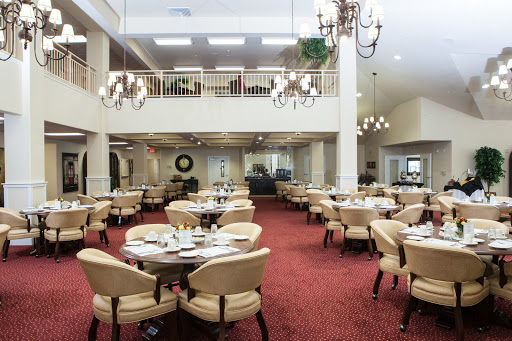 A spacious and elegantly designed dining room featuring round tables and comfortable chairs, adorned with chandeliers.