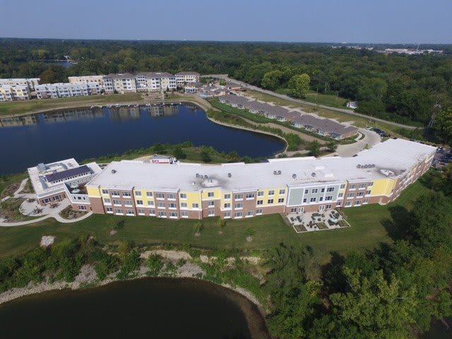 Aerial view of a large residential building situated beside a scenic lake and surrounded by greenery.