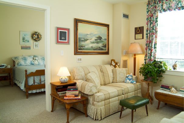 A cozy living room with vintage decor including a sofa, lamp, painting, and side table with books.