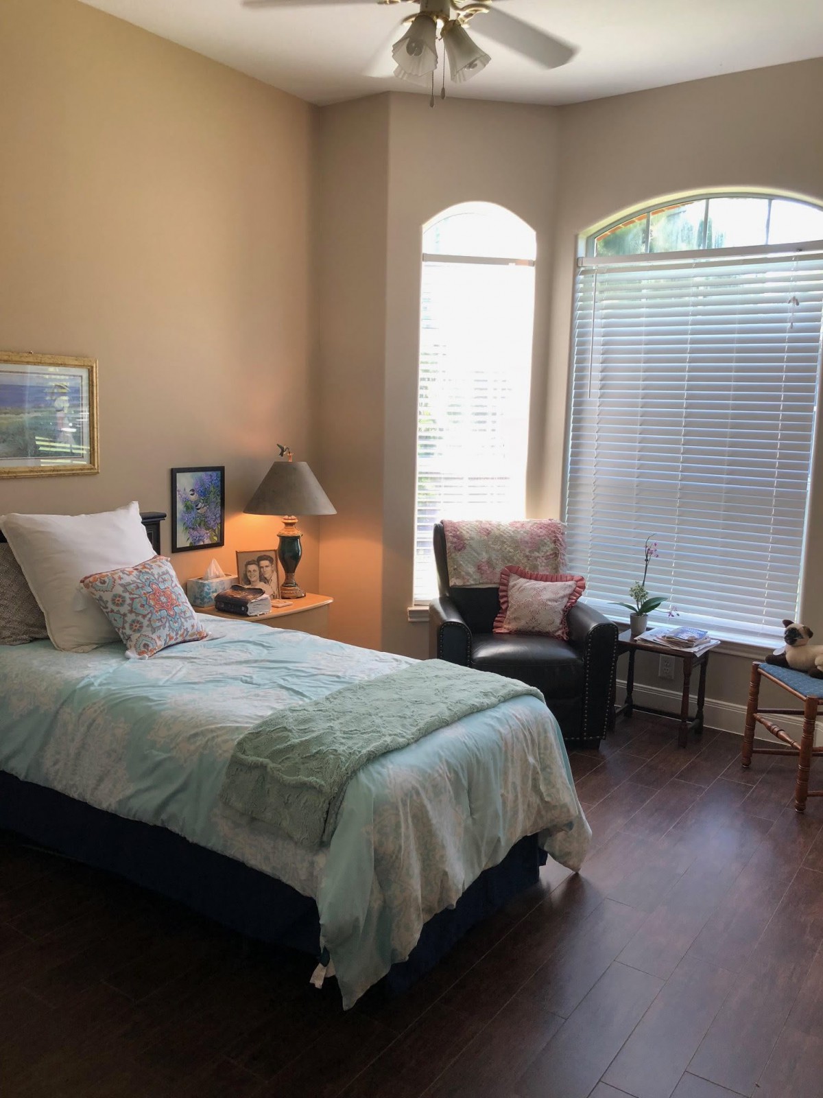 A cozy bedroom with a single bed, large windows, and warm decor.