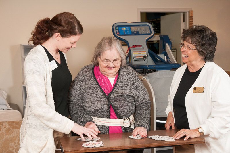 An elderly woman is engaged in a rehabilitation activity with the assistance of two healthcare workers.