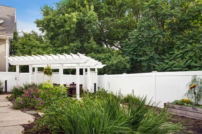 A serene garden with a white pergola and fence, surrounded by lush greenery.