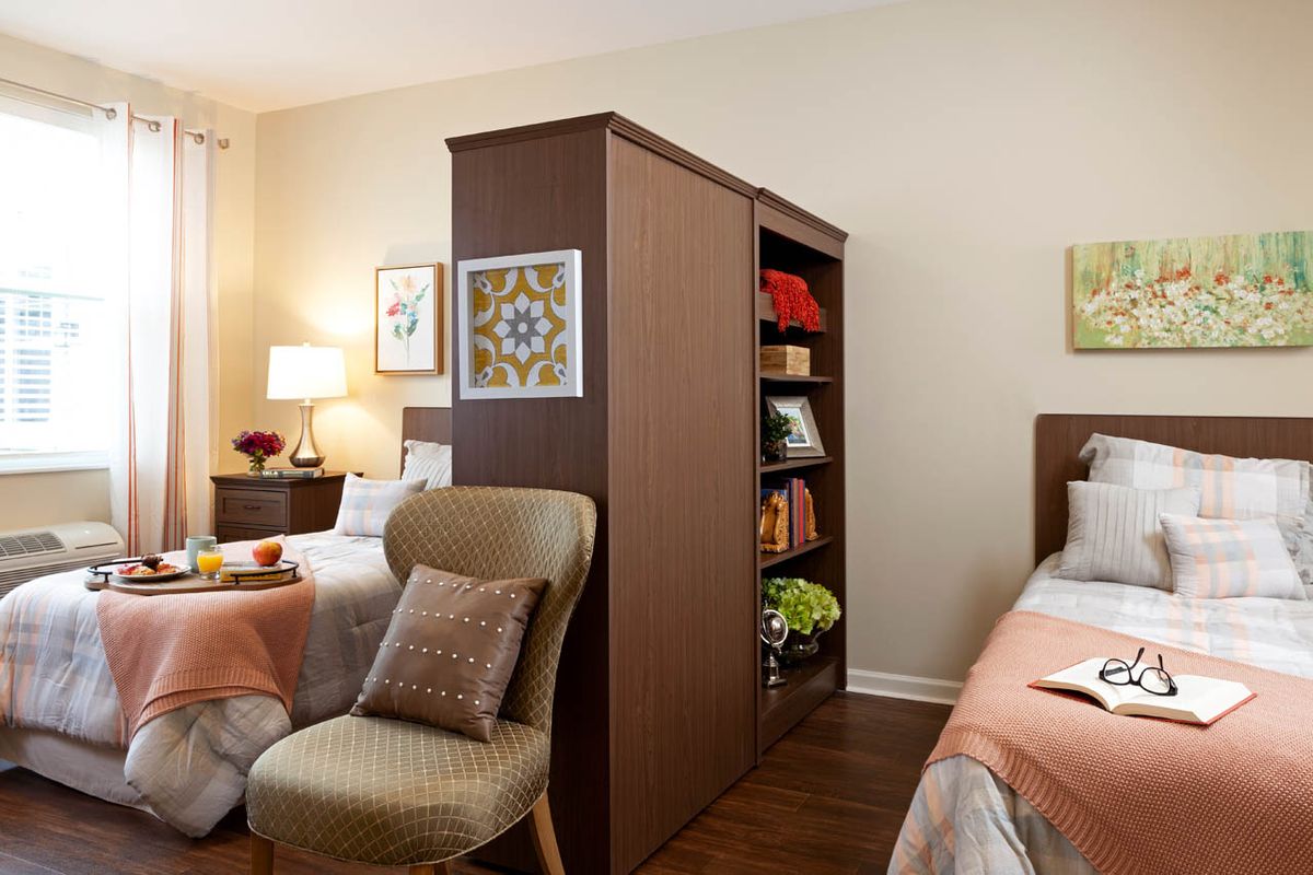 A shared bedroom featuring two beds separated by a central bookshelf, with cozy decor and warm lighting.