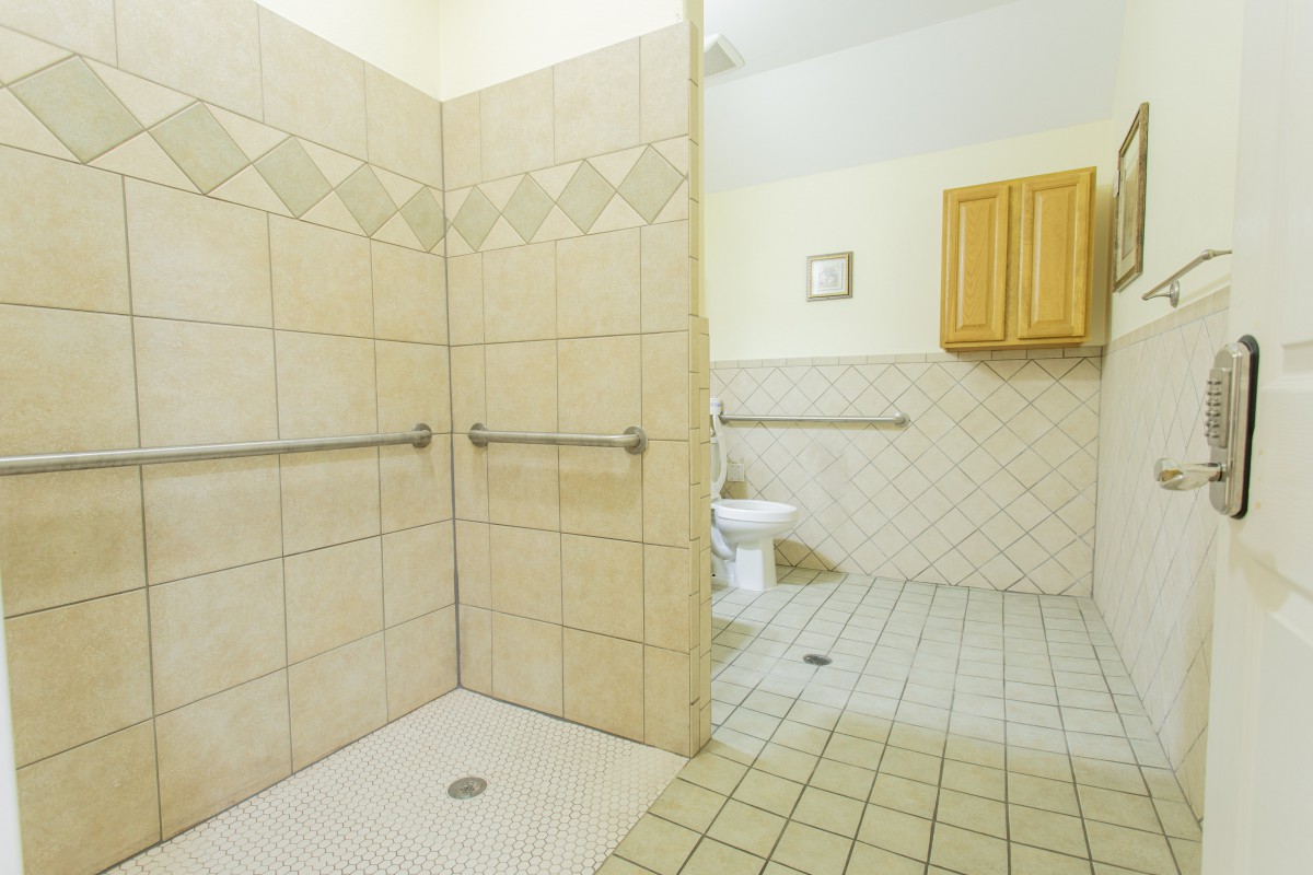 An accessible bathroom featuring a shower area with grab bars and tiled walls and floor.