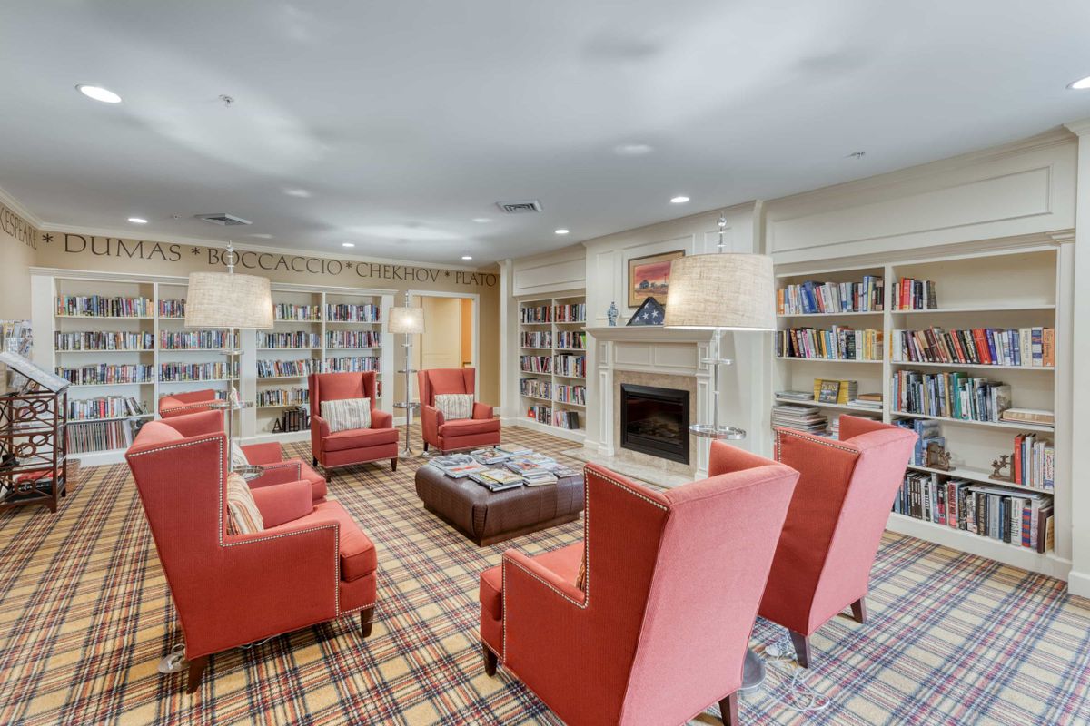 A cozy library reading area with red chairs and a fireplace.