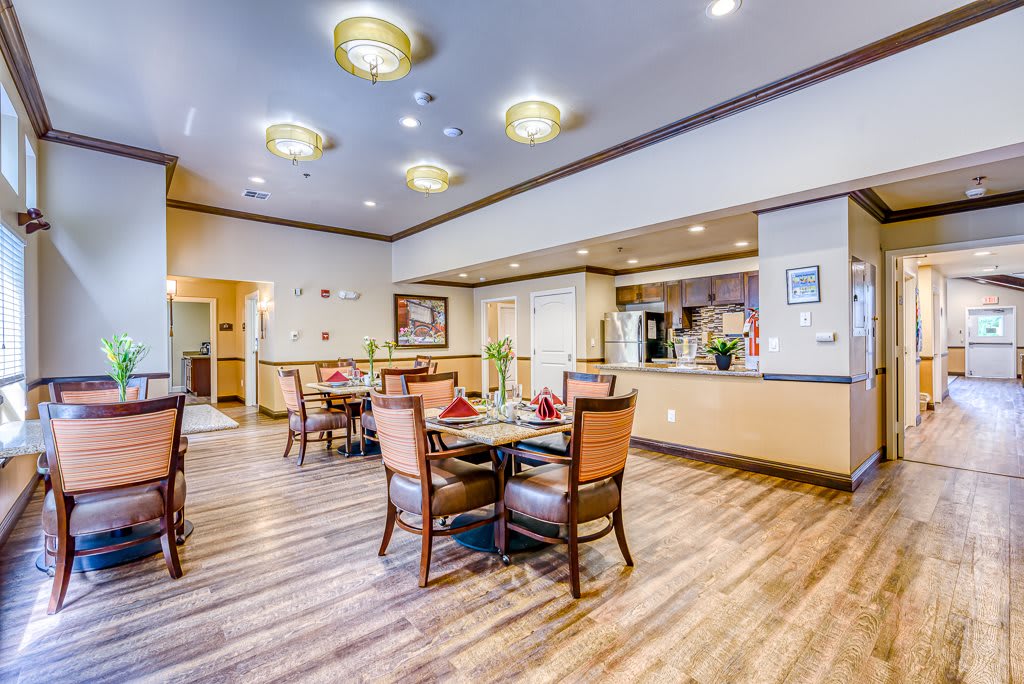 A well-lit dining room with wooden flooring, featuring tables and chairs arranged neatly.