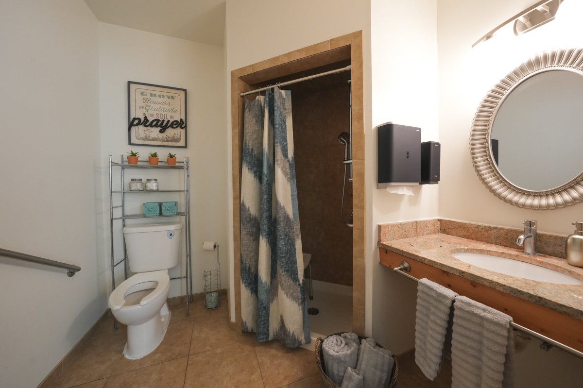 A clean and organized bathroom with a shower, toilet, sink, and shelving unit.