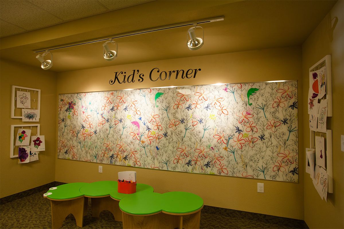 A children's play space called 'Kid's Corner' featuring a colorful and artistic wall, accompanied by green tables.