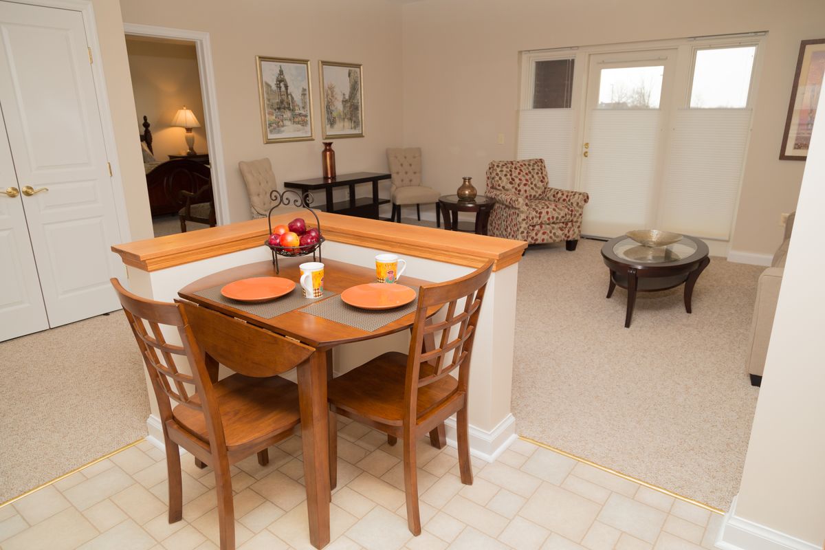 A cozy apartment interior featuring a small dining area with a wooden table and chairs, leading into a living room with comfortable seating.