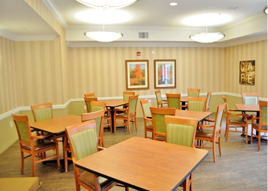 An empty dining room with wooden tables and chairs, softly lit from above.