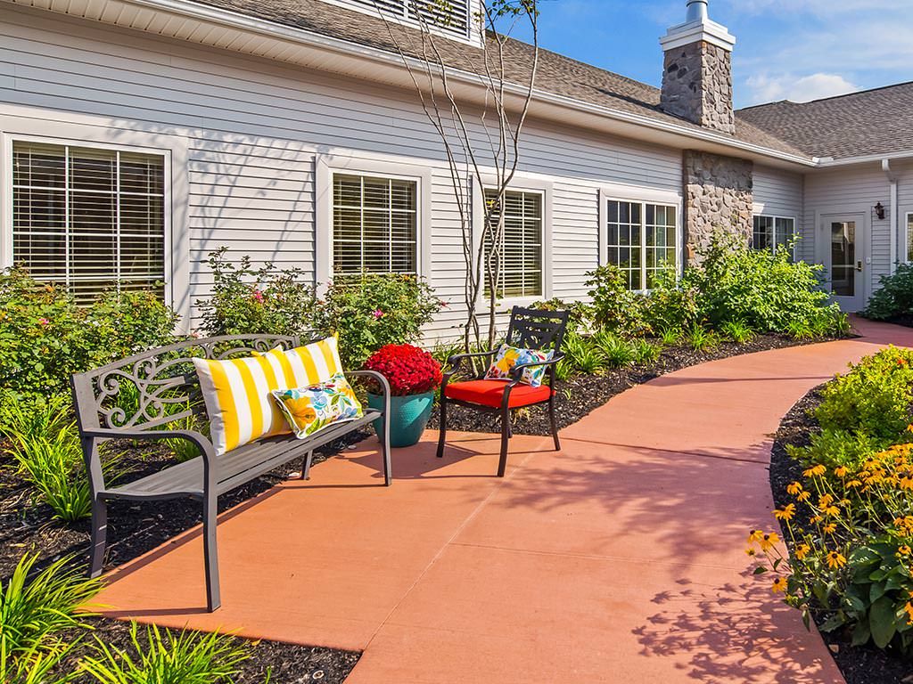 A cozy patio with colorful cushions on benches, surrounded by lush greenery and bright flowers.