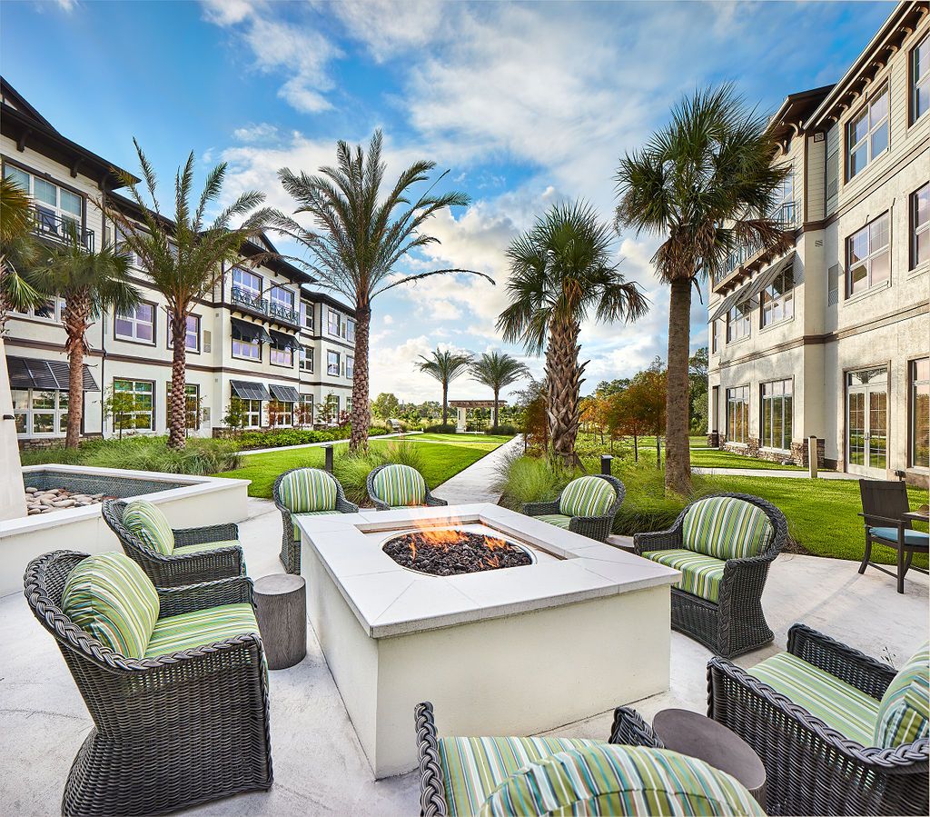 A modern apartment complex with a cozy outdoor seating area and a fire pit surrounded by palm trees.