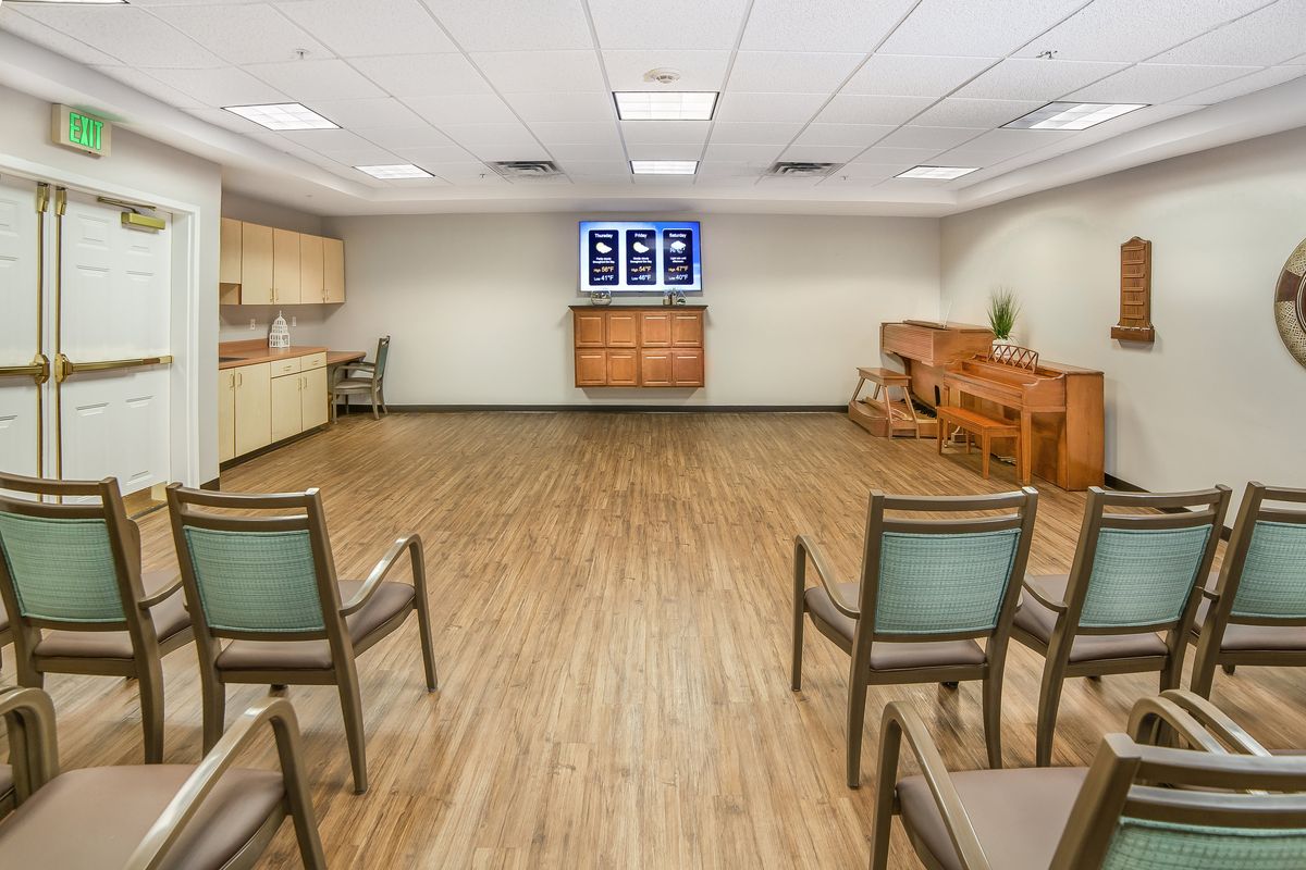 A well-lit meeting room with wooden floors, arranged with several chairs and a television mounted on the wall.