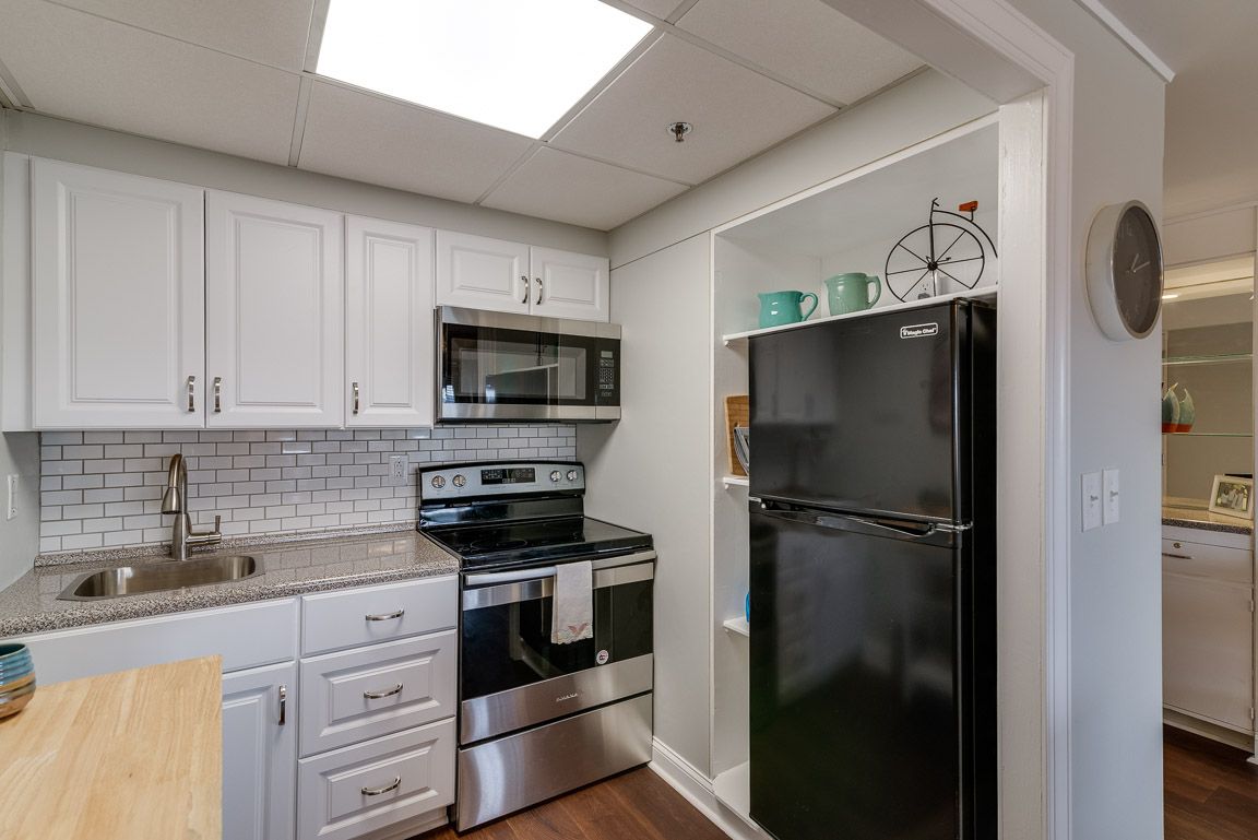 A modern kitchen with white cabinets, a black refrigerator, and stainless steel appliances.