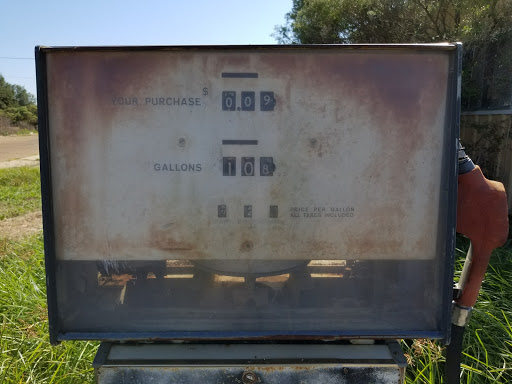 A weathered and rusty sign indicating electrical connections or measurements.