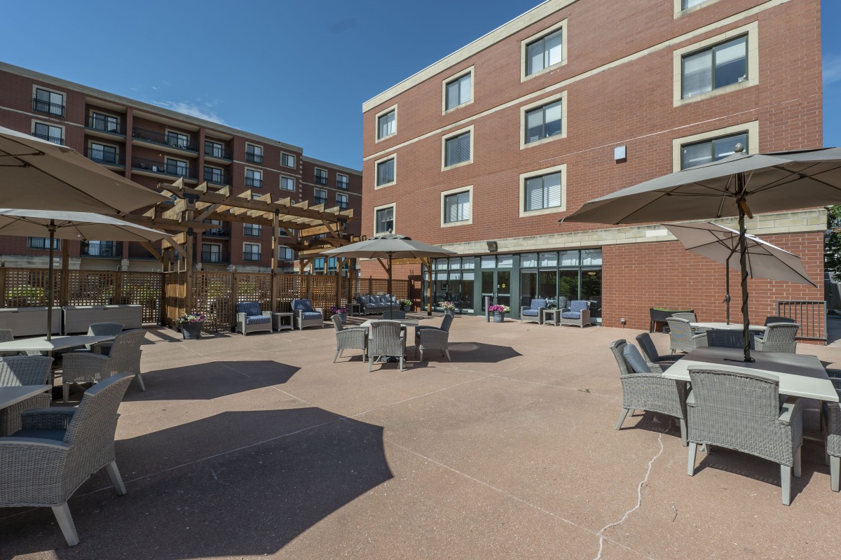 A sunny outdoor patio area with chairs and tables near a brick building.