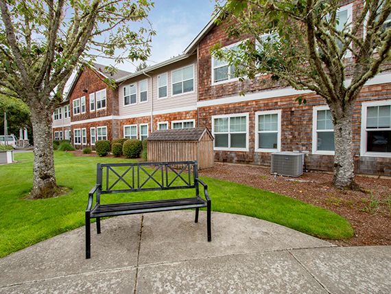 A bench sits in front of a brick building surrounded by trees and a well-maintained lawn.