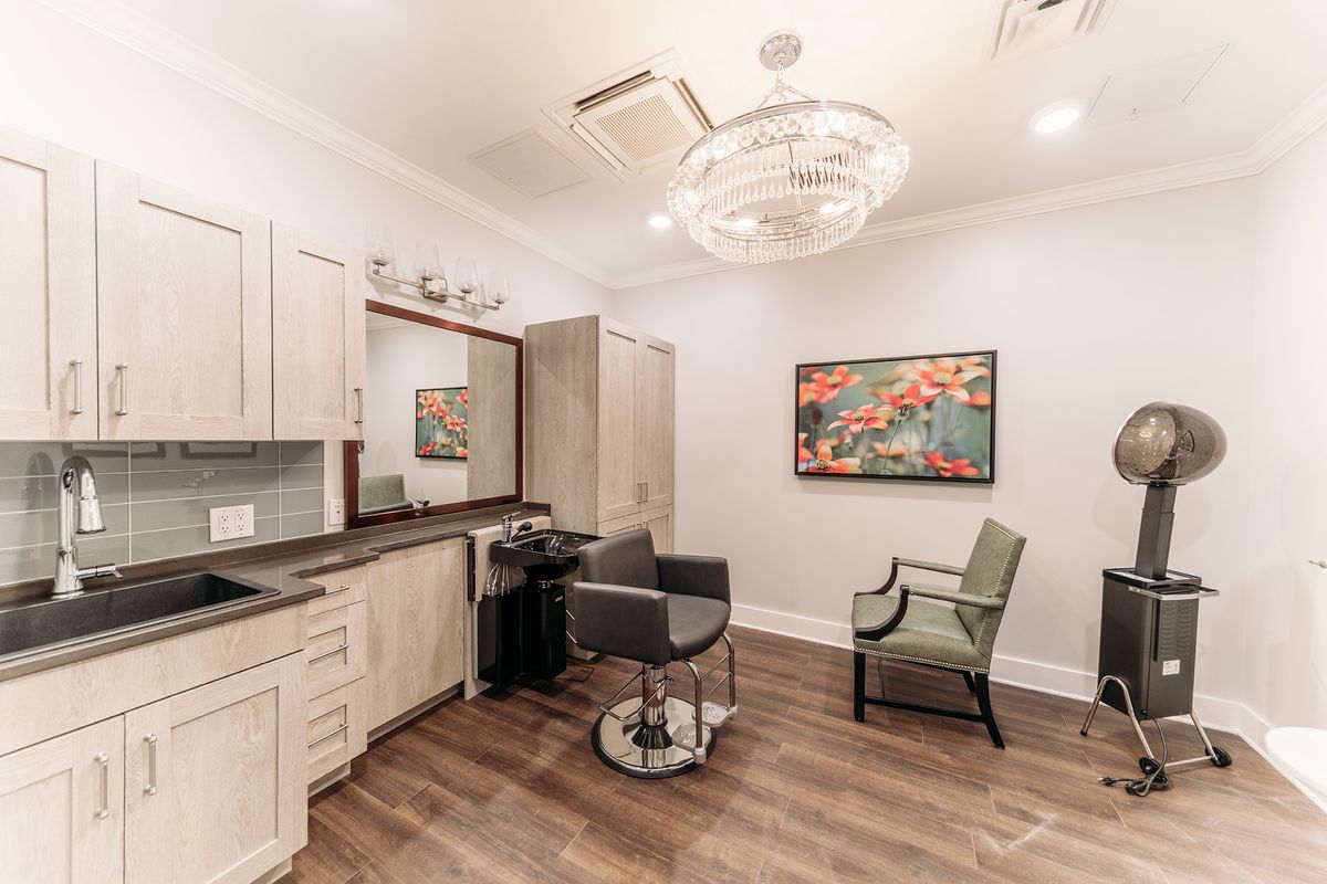 A modern hair salon with stylish furnishings, featuring a chandelier and a large mirror.