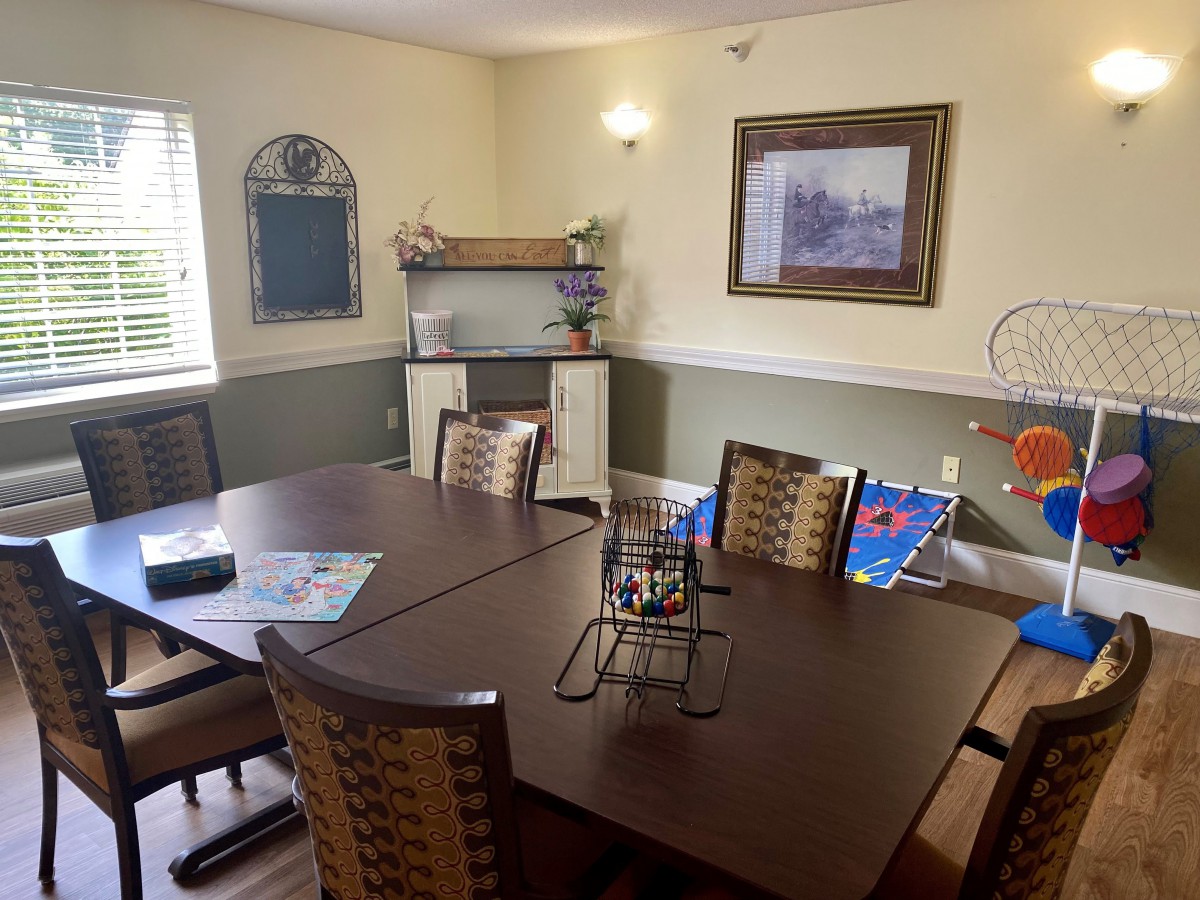 A cozy dining room with a large table and several chairs, decorated with artwork and shelves.
