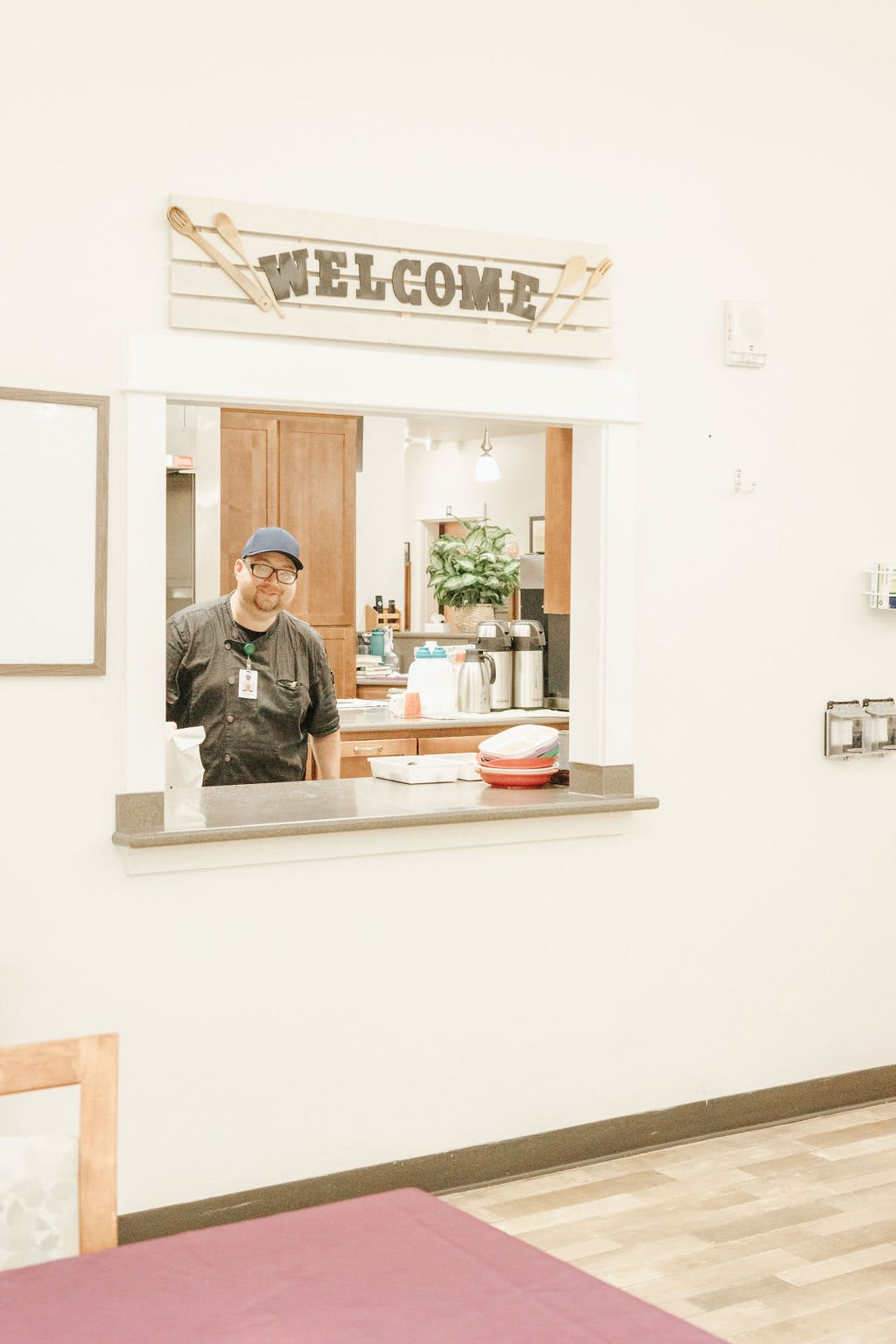 Person standing behind a kitchen counter with a welcome sign.