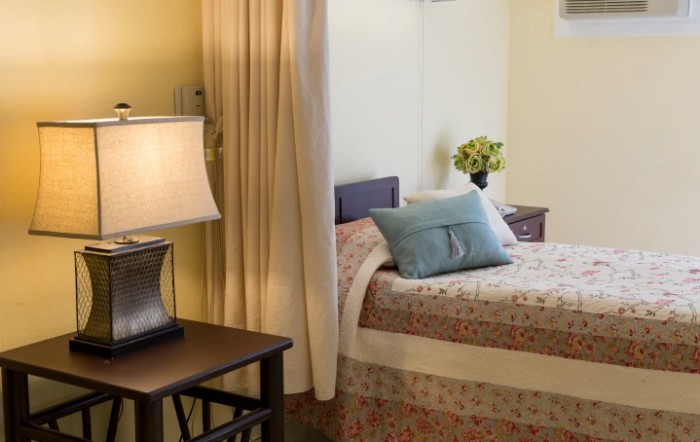 A cozy bedroom with a single bed, a decorative cushion, and a lamp on the nightstand.