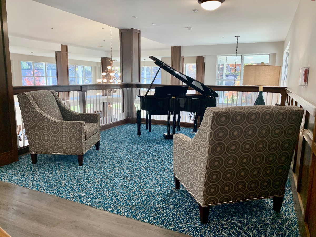 A cozy seating area featuring a grand piano and two patterned chairs on a blue carpet.