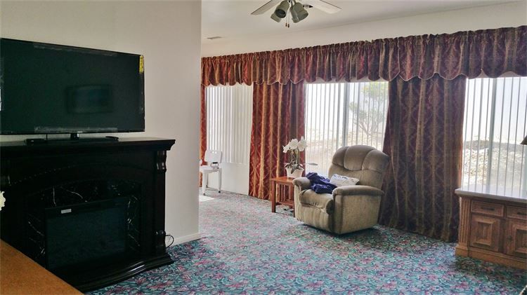 A cozy living room with an armchair next to large windows and a television above the fireplace.