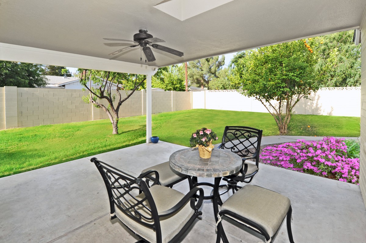 A cozy outdoor patio with a table and chairs, surrounded by a lush green garden.