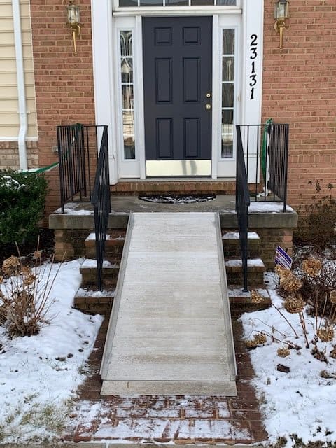A ramp leading to the front entrance of a brick house with snow on the ground.